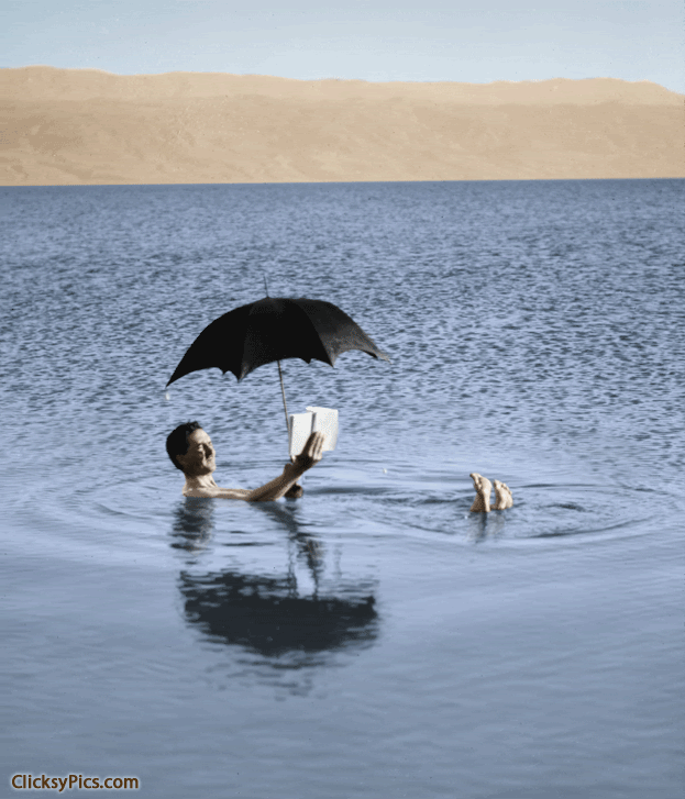 1900-1920 - Around the Dead Sea. Man floating with book and umbrella in hands.